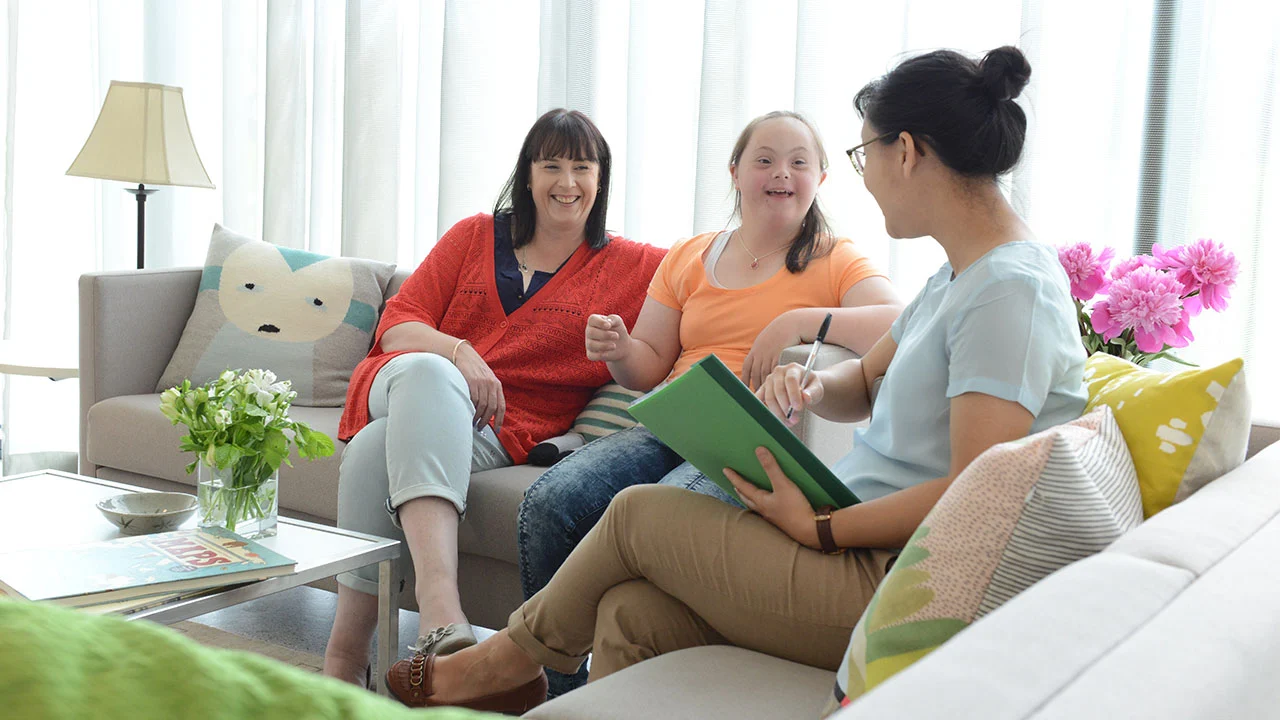 Urcare support worker chatting with a participant and her family at home